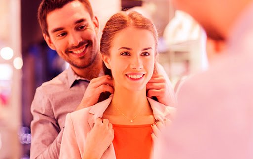 Experiência do consumidor Imagem representando a Experiência do cliente, contendo uma mulher experimentando um colar, com a ajuda de um homem em uma loja física.